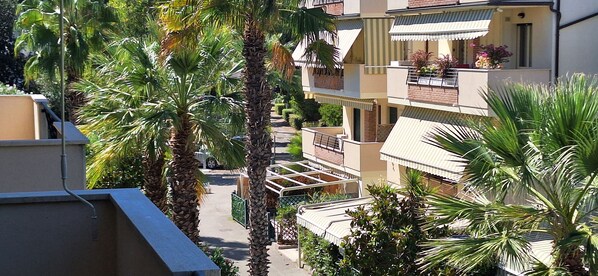 A residential building with multiple balconies, surrounded by palm trees and other greenery.