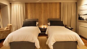 A hotel room with two beds, a ceiling fan, a nightstand, a chair, and a window with curtains. - Club Hotel Catedral (San Carlos de Bariloche)