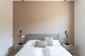 A bedroom with a bed, two bedside tables, two lamps, and a plain wall. - Rebo apartment in Puegnago del Garda with pool (Puegnago sul Garda)