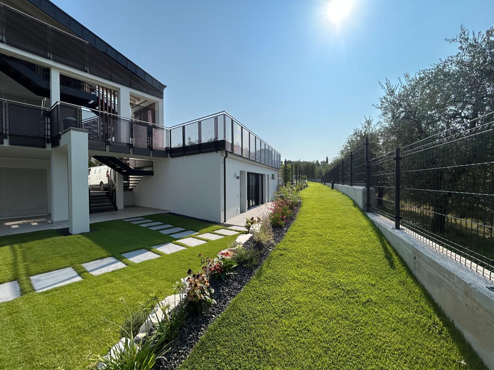 A modern building with a flat roof, a balcony, and a well-maintained lawn with stepping stones.
