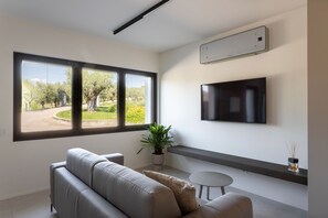 Una sala de estar moderna con un sofá gris, una mesita redonda, una planta en maceta y un televisor montado en la pared.
