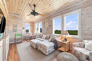 A spacious room with a large bed, two sofas, a dining table, and a ceiling fan. - The Beach House #226 - Luxury 8-Bedroom Oceanfront Rental w/ Private Pool (North Topsail Beach)
