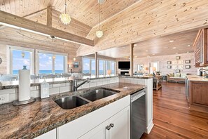 A spacious kitchen with granite countertops, stainless steel appliances, and wooden flooring. - The Beach House #226 - Luxury 8-Bedroom Oceanfront Rental w/ Private Pool (North Topsail Beach)