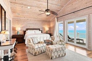 A spacious bedroom with a large bed, two armchairs, a desk, and a balcony with a view of the ocean. - The Beach House #226 - Luxury 8-Bedroom Oceanfront Rental w/ Private Pool (North Topsail Beach)