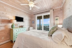 Ein Schlafzimmer mit einem Bett, einem Schminktisch, einem Fernseher und einem Fenster mit Blick auf das Meer.