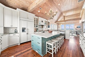 A spacious kitchen with wooden flooring, white cabinetry, and a large island with stools. - The Beach House #226 - Luxury 8-Bedroom Oceanfront Rental w/ Private Pool (North Topsail Beach)