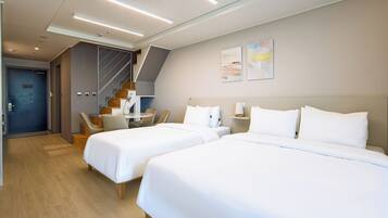A hotel room with two beds, a desk, a chair, a staircase, and artwork on the wall.