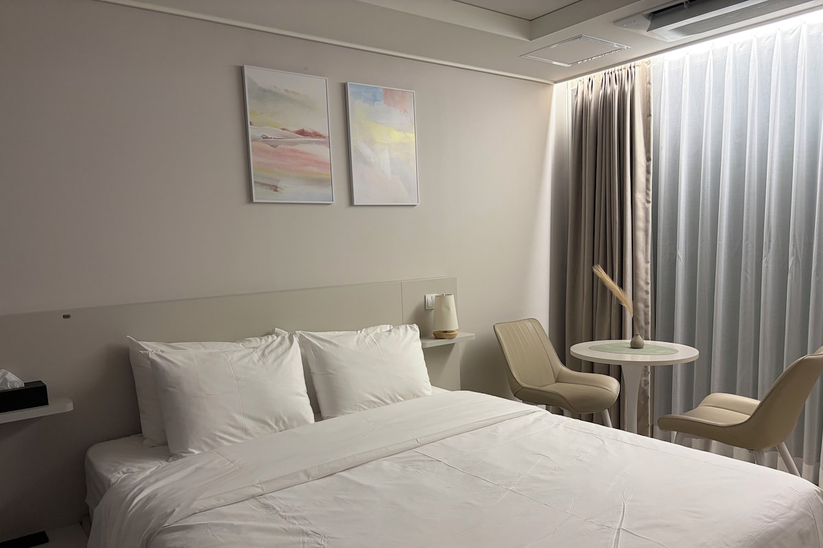 Una habitación de hotel con una cama, dos sillas, una mesita y una lámpara.