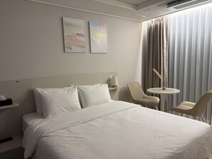 Una habitación de hotel con una cama, dos sillas, una mesita y una lámpara.