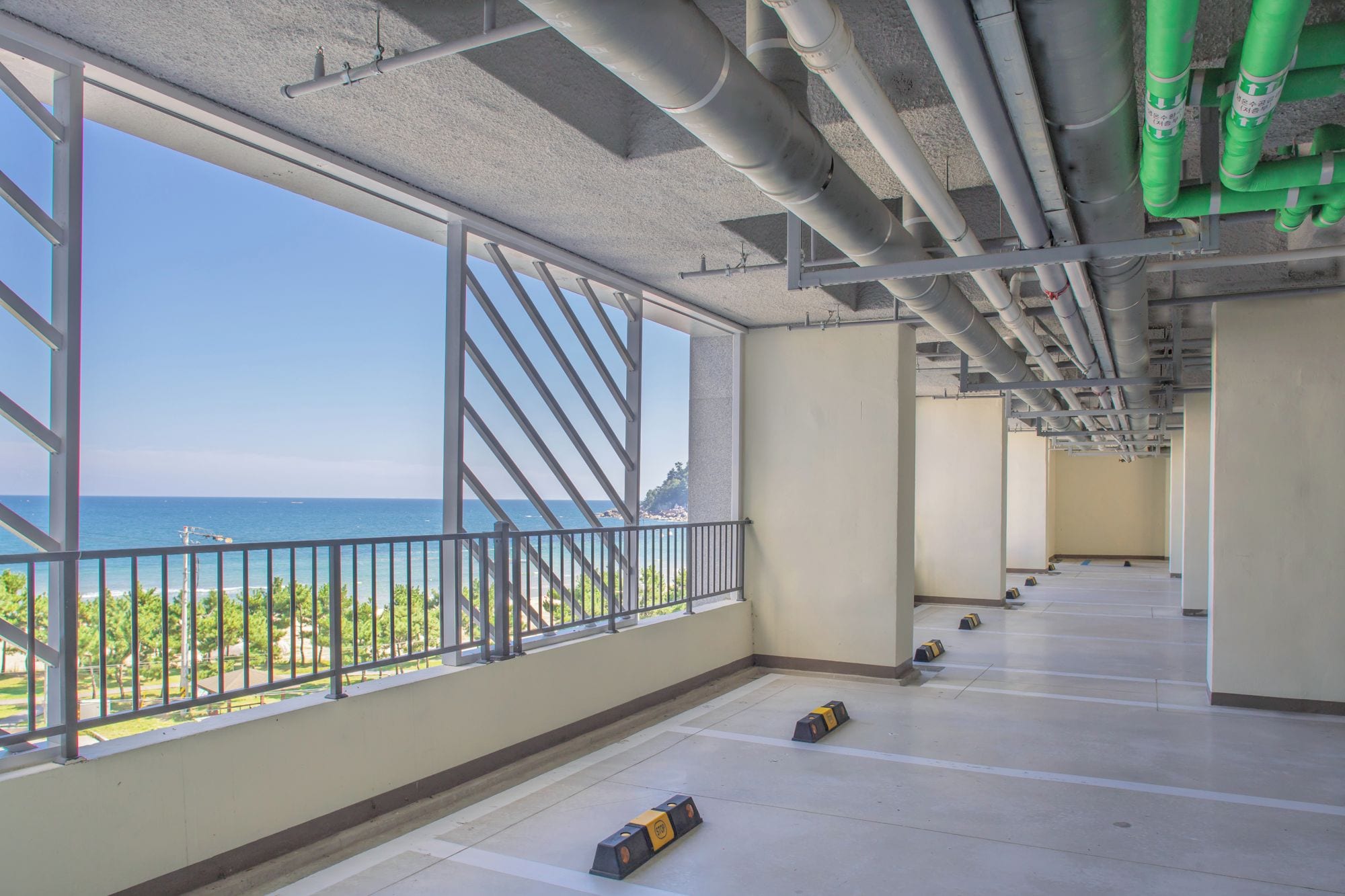 An interior space with large windows overlooking a beach, visible pipes on the ceiling, and a clear view of the ocean.