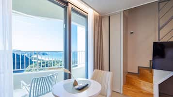 Habitación de hotel moderna con balcón, una mesa redonda, un sofá y una televisión.