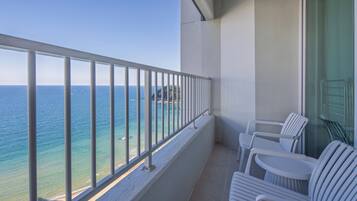 A balcony with a metal railing, white plastic chairs, and a view of the sea.