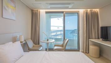 A hotel room with a bed, two chairs, a small table, a TV, and a balcony with curtains.