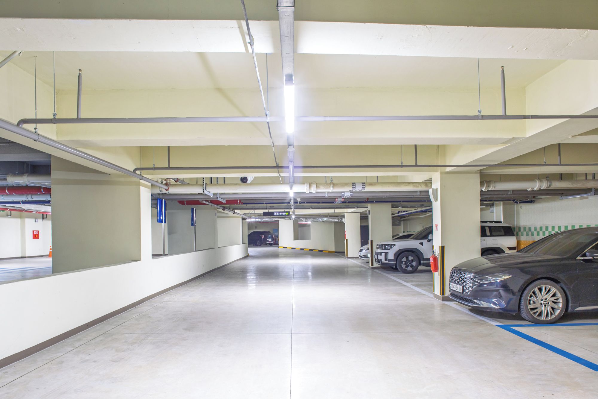 Garagem de estacionamento com vários níveis, sinalização clara, extintor de incêndio e marcação de vaga azul.