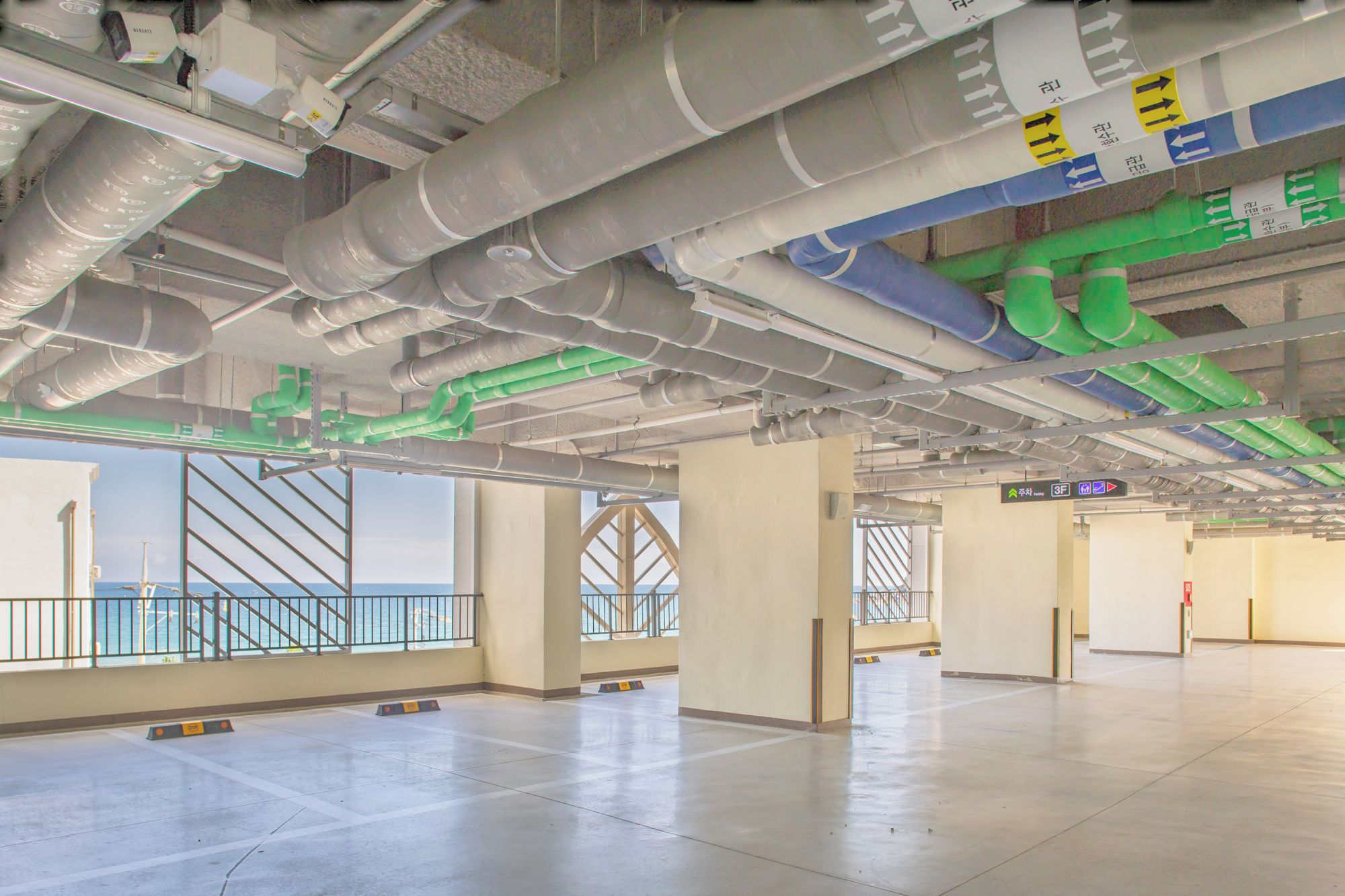 Espacio interior con columnas estructurales visibles, tuberías en el techo y señalización direccional.