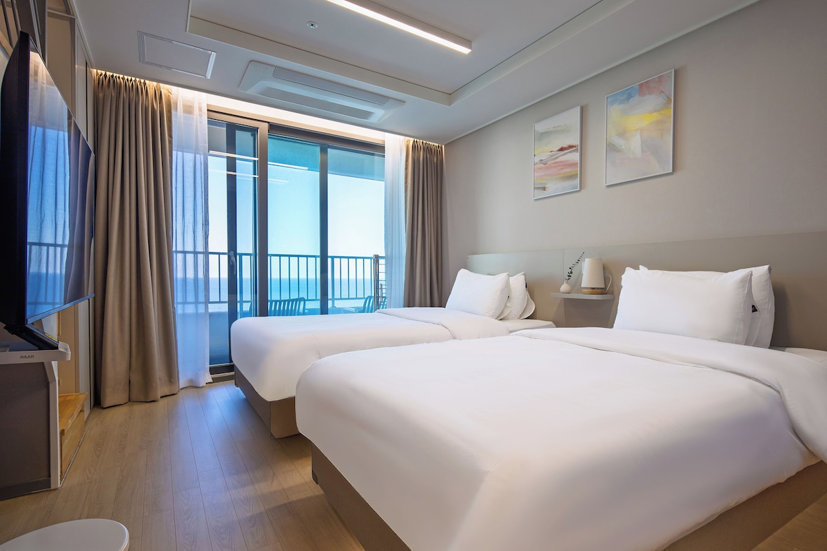 A hotel room with two beds, a TV, a desk, and a balcony with a view.