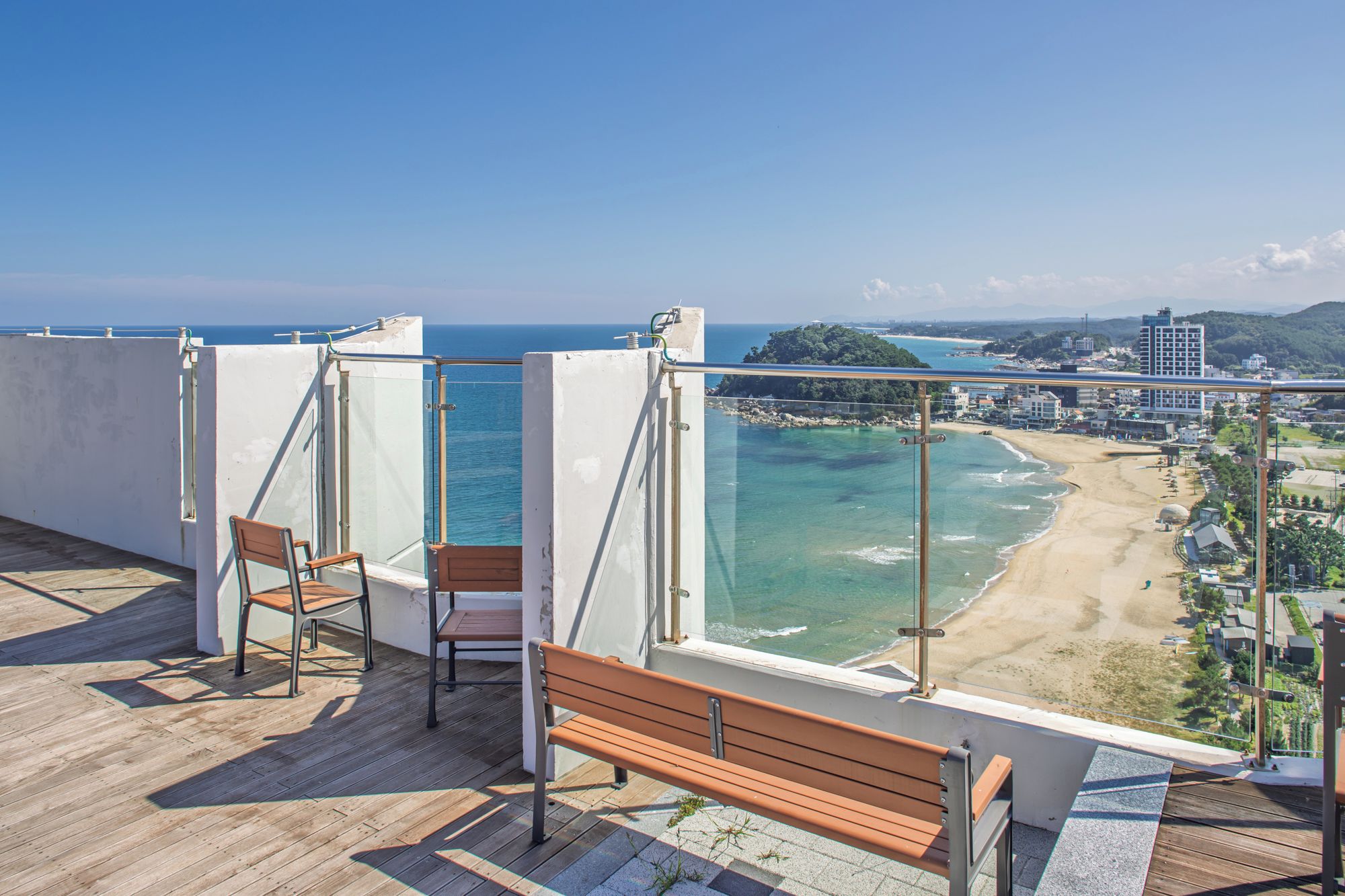 A balcony with a wooden floor, two wooden chairs, and a bench.