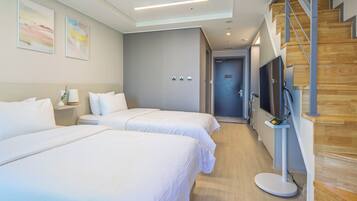 A hotel room with two beds, a TV, a desk, and a staircase.