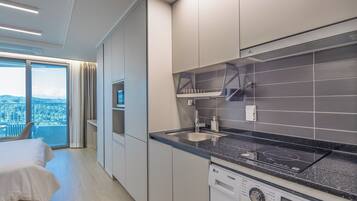 Habitación de hotel moderna con balcón, kitchenette y un amplio ventanal con vistas a la ciudad.