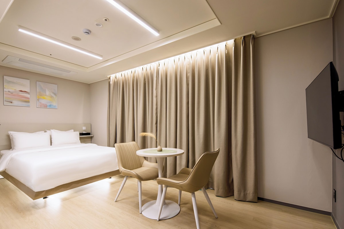 A hotel room with a bed, two chairs, a small table, and a TV.