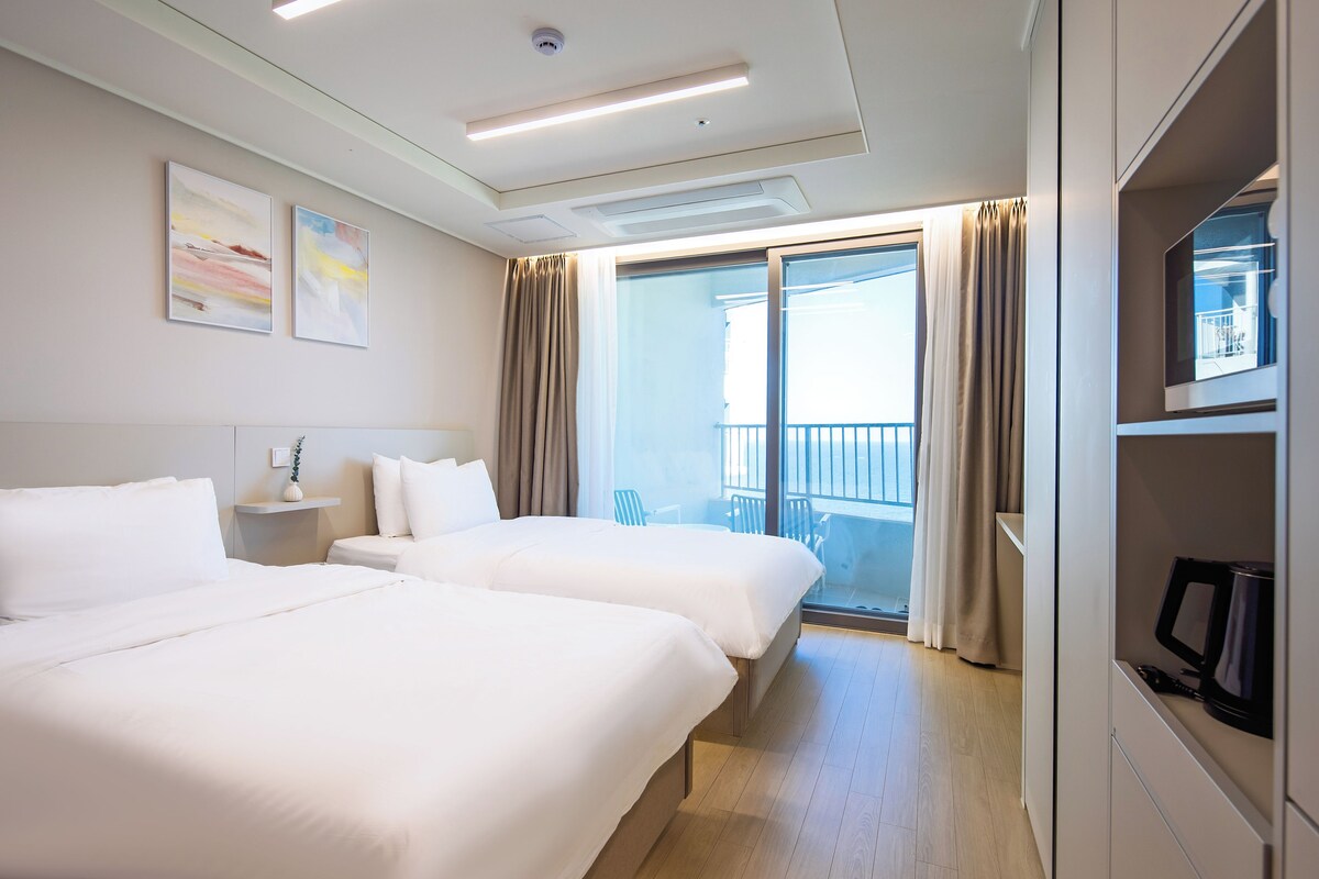 A hotel room with two beds, a television, a balcony with curtains, and artwork on the wall.