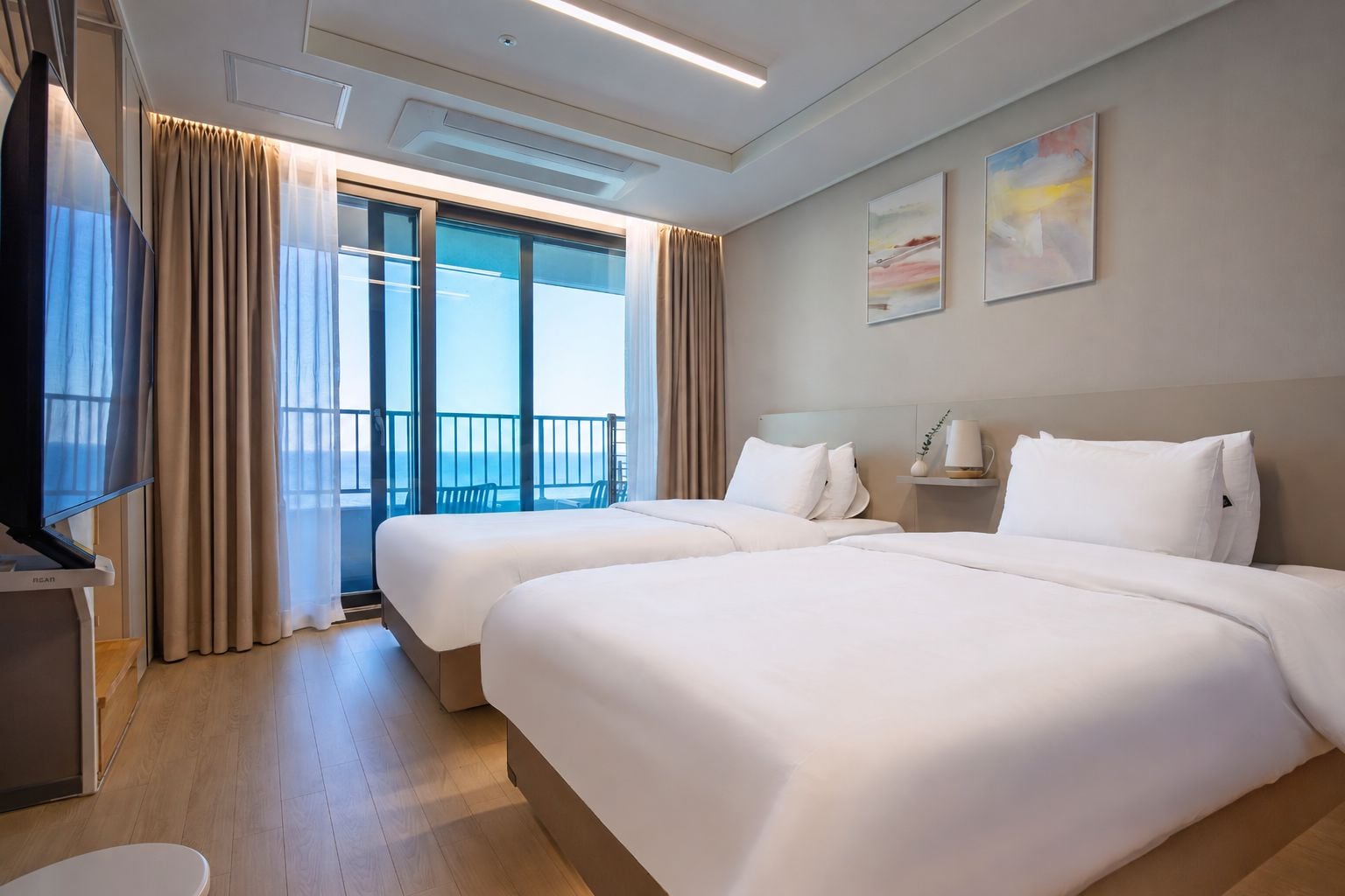 A hotel room with two beds, a TV, and a balcony with curtains.