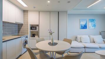 A modern kitchen with built-in appliances, a dining area with a round table and chairs, and a living area with a sofa and abstract wall art.