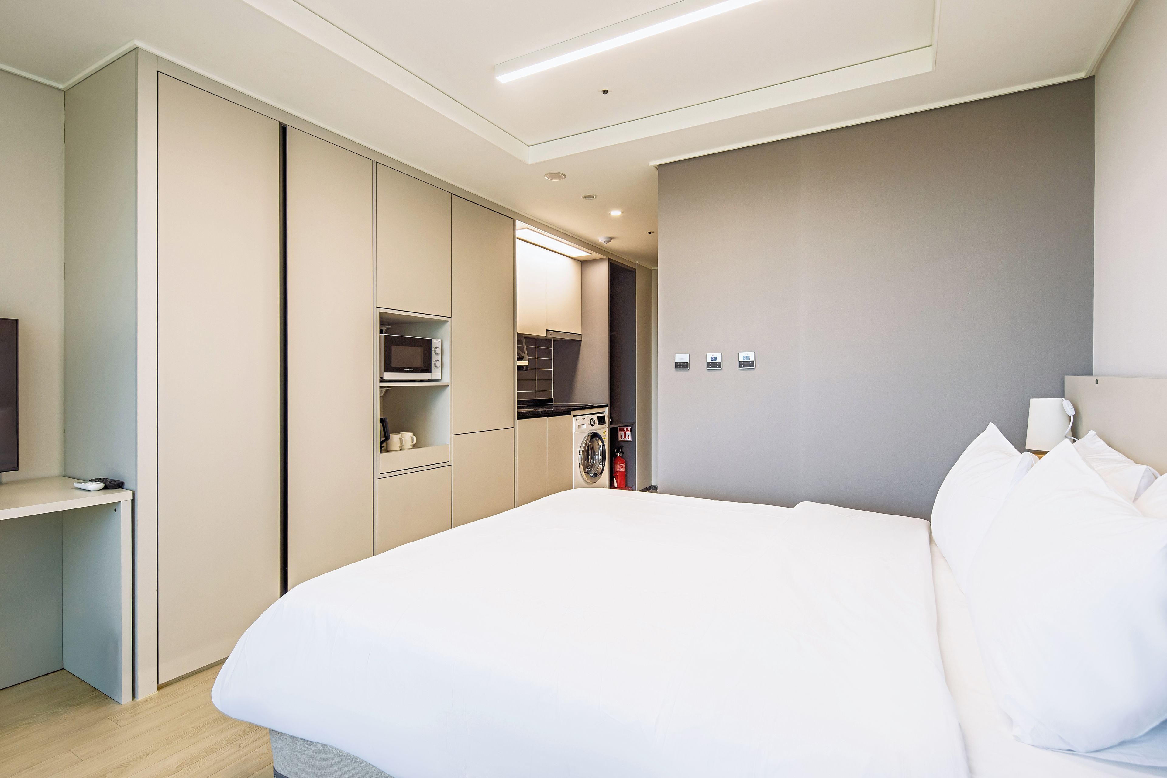 Habitación de hotel con cama, escritorio, microondas, lavadora y extintor.