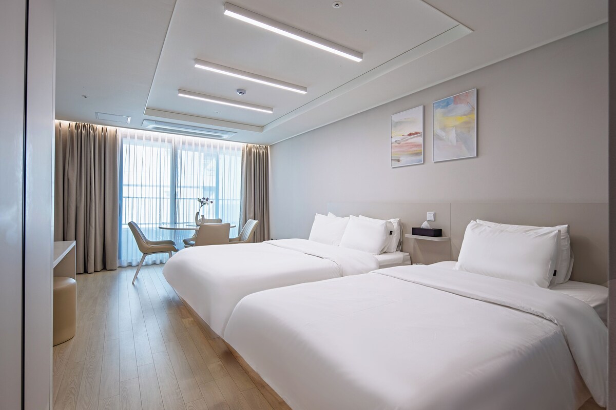 A hotel room with two beds, a desk, and a chair.