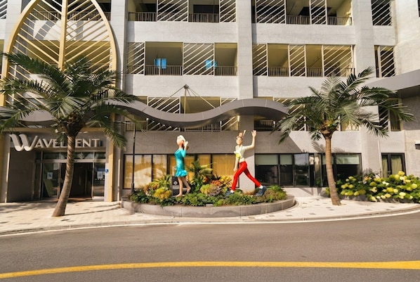 Entrada de hotel con fachada moderna, palmeras y dos estatuas.