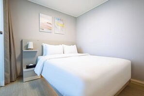 Habitación de hotel con una cama grande, una mesita de noche, una lámpara y dos cuadros en la pared.