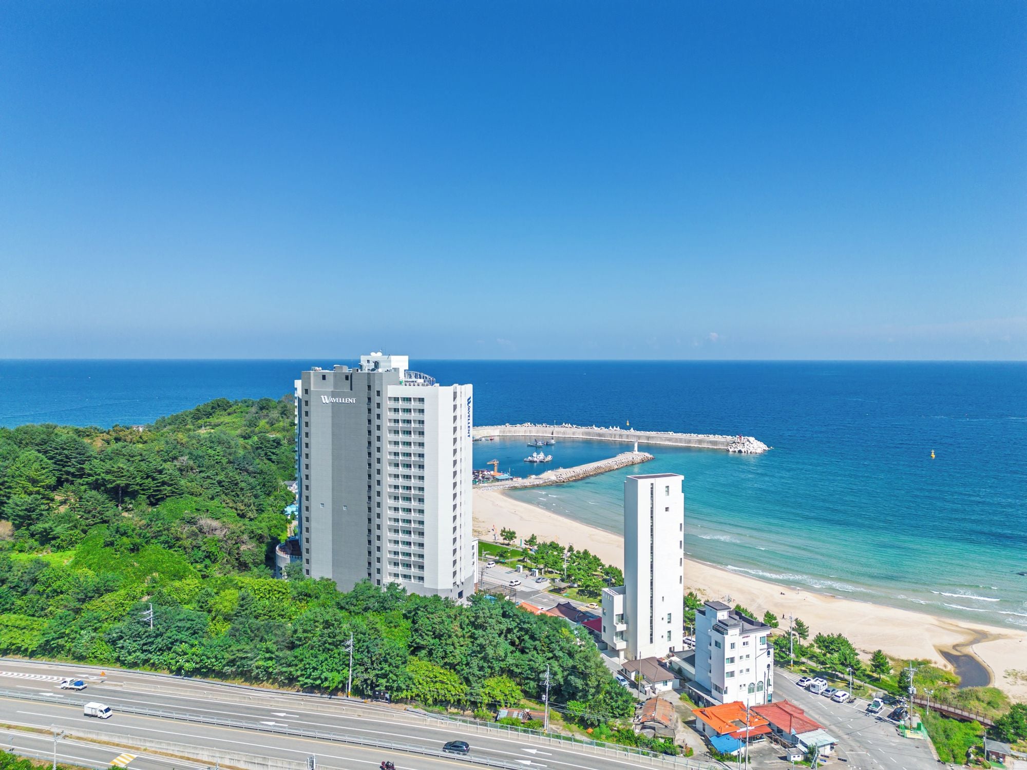 A coastal cityscape with high-rise buildings, a beach, and a clear blue sky.