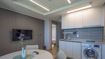 A modern hotel room with a dining area, a TV, a washing machine, and a bathroom visible through an open door.
