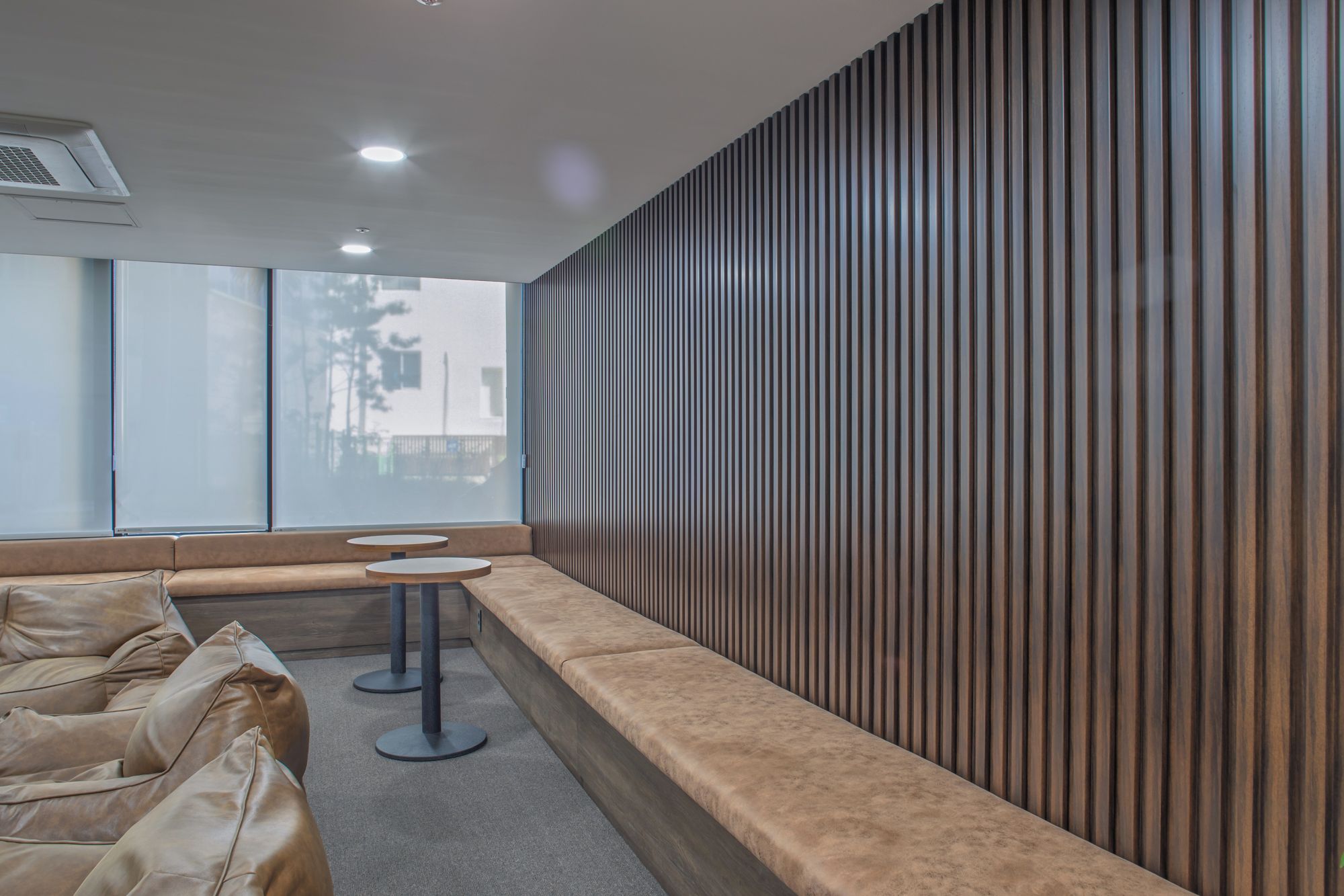 A waiting area with a long bench, two round tables, and a wooden slatted wall.