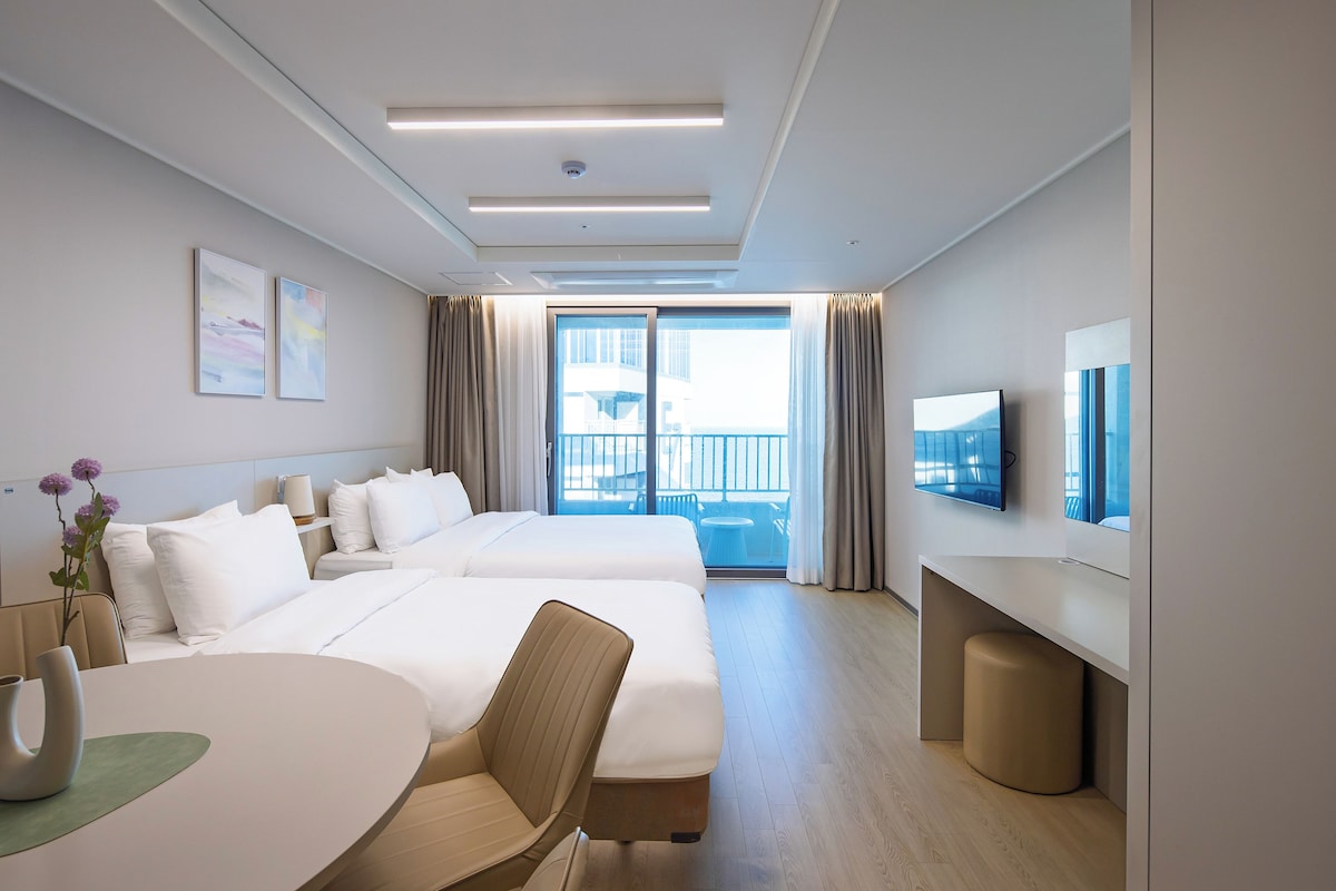 A hotel room with two beds, a TV, a balcony with a view, and a dining area.