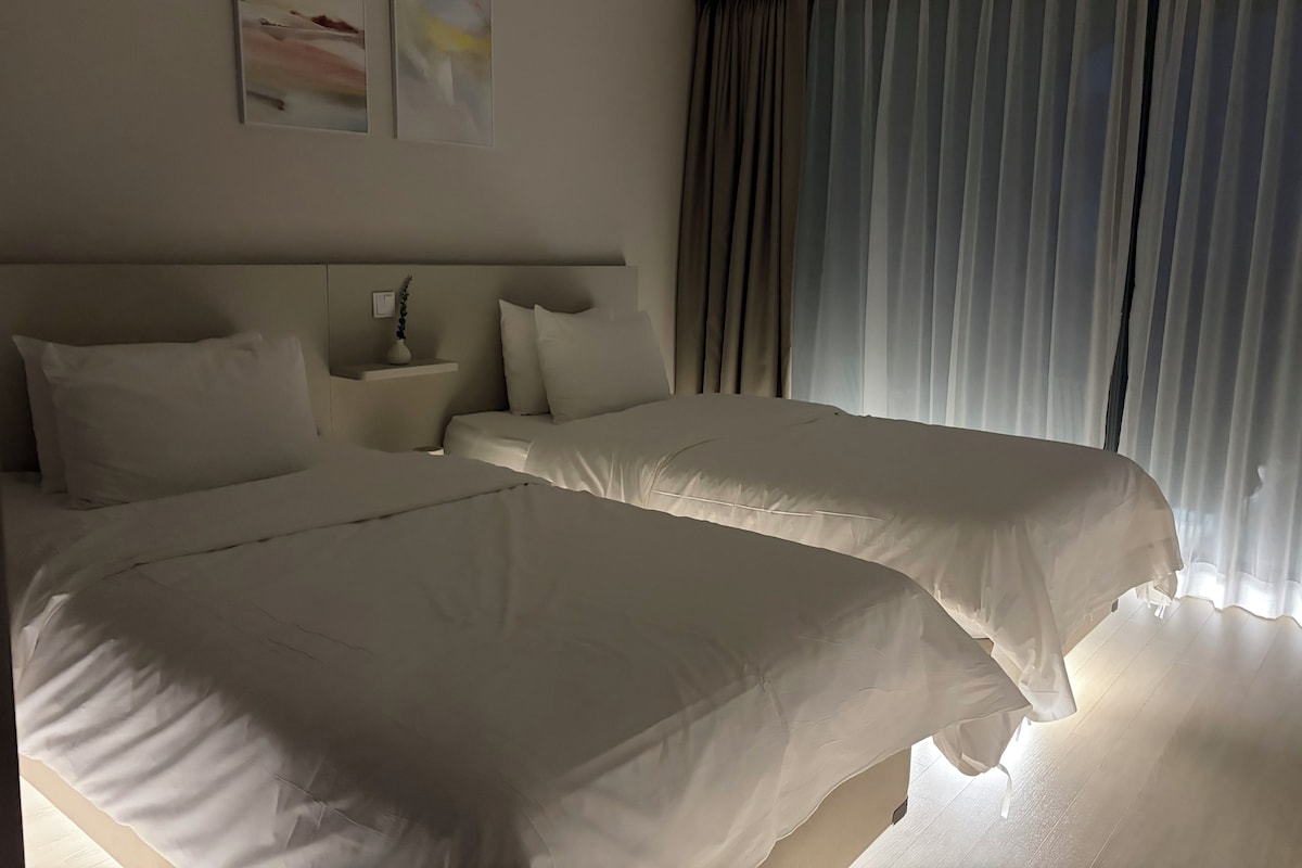 Una habitación de hotel con dos camas, una mesita de noche y una ventana con cortinas.