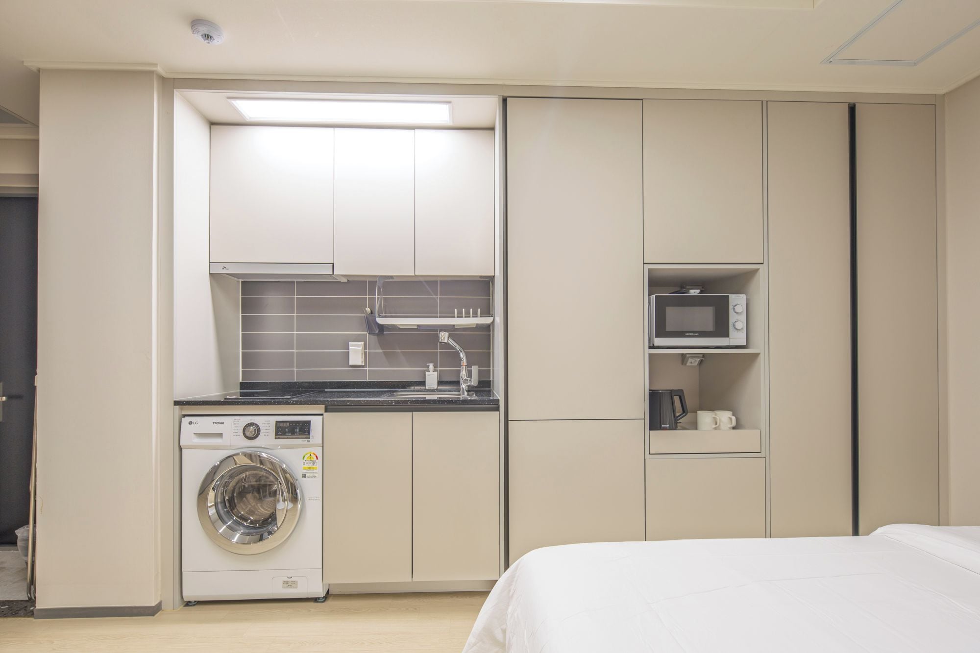 A compact hotel room with a washing machine, microwave, and a bed.