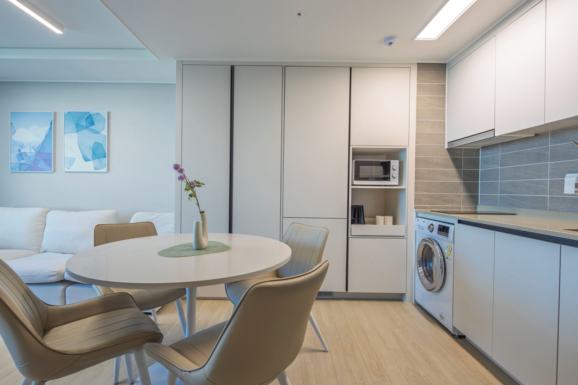 A modern kitchen with a built-in washing machine, a dining area with a round table and chairs, and a small seating area with a sofa.