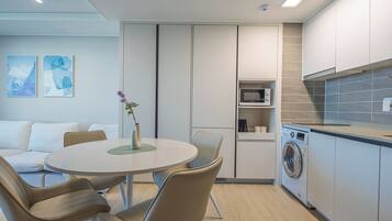 A modern kitchen with a built-in washing machine, a dining area with a round table and chairs, and a small seating area with a sofa.