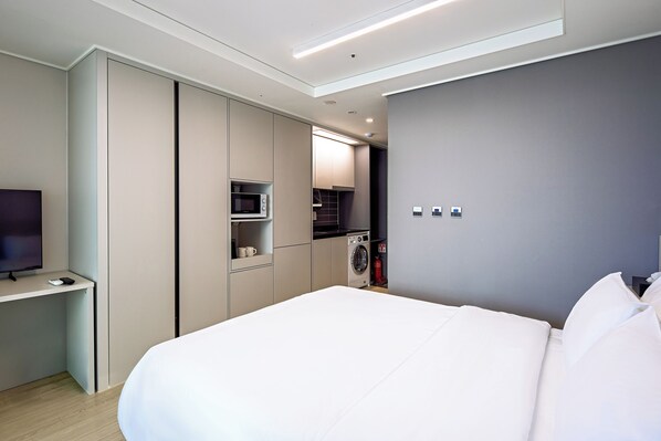 A modern hotel room with a bed, a TV, a microwave, and a washing machine.