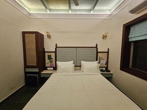 Habitación de hotel con cama, dos mesitas de noche, una lámpara de pared y una ventana con persiana.