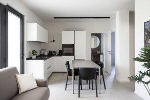 A modern kitchen with white cabinets, a dining table with chairs, a built-in oven, and a coffee maker. - Apartment Groppello Casa Franzosiwith pool (Puegnago sul Garda)