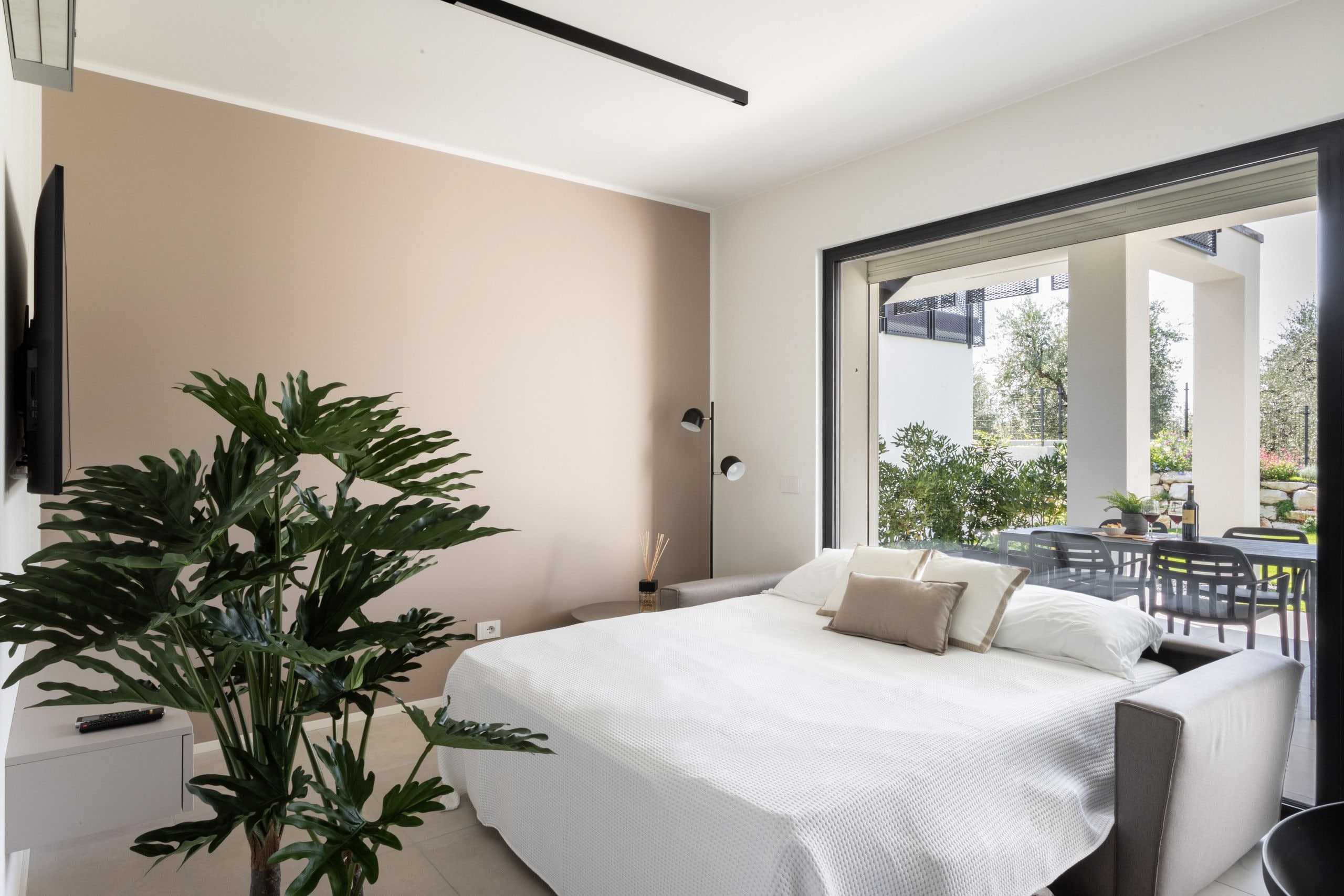 Un dormitorio moderno con una cama grande, una planta en maceta y vistas al patio exterior.