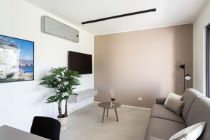 A modern living room with a sofa, a dining table, a potted plant, a flat-screen TV mounted on the wall, and a small side table. - Apartment Groppello Casa Franzosiwith pool (Puegnago sul Garda)