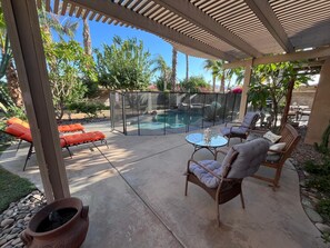 Ein überdachter Außenbereich mit Pool, Liegestühlen und einem Tisch.
