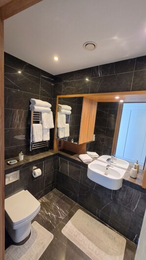 A modern bathroom with a toilet, two sinks, a mirror, and a towel rack. - Luxury Canary Wharf Skyline Apartment (London)