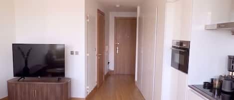 Un apartamento moderno con sala de estar, televisor, sofá, cocina y pasillo.