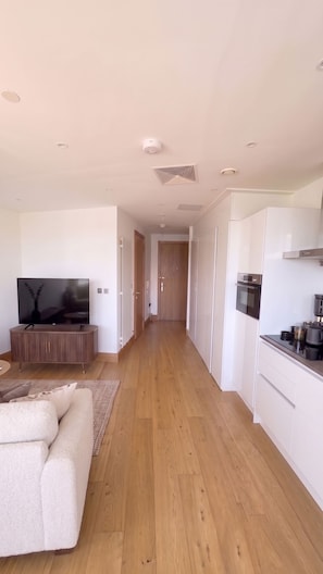 A modern apartment with a living room, a TV, a sofa, a kitchen, and a hallway. - Luxury Canary Wharf Skyline Apartment (London)