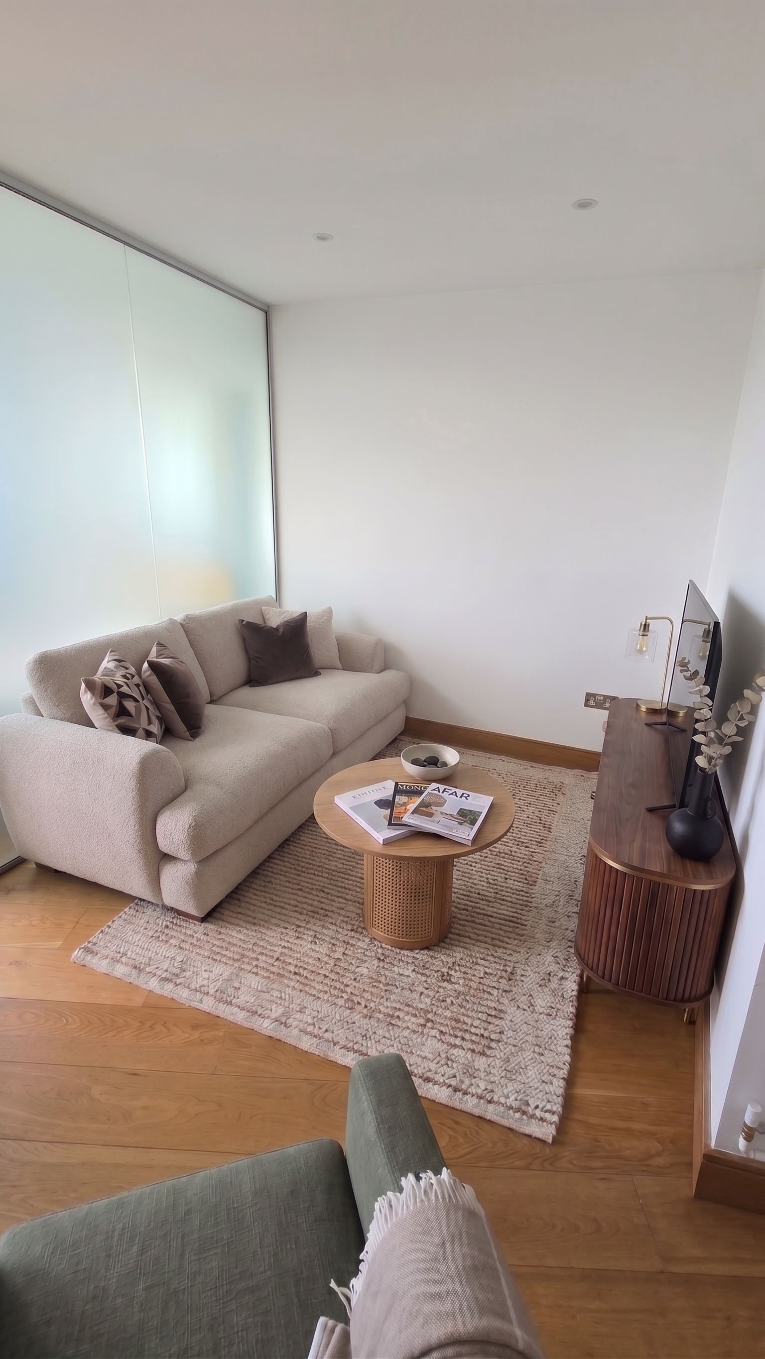 Una sala de estar moderna con un sofá, una mesa de centro, una mesita auxiliar y un televisor.