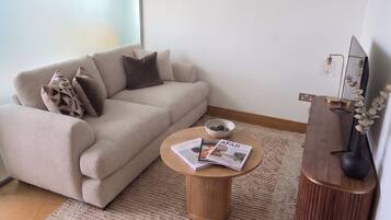 Una sala de estar moderna con un sofá, una mesa de centro, una mesita auxiliar y un televisor.